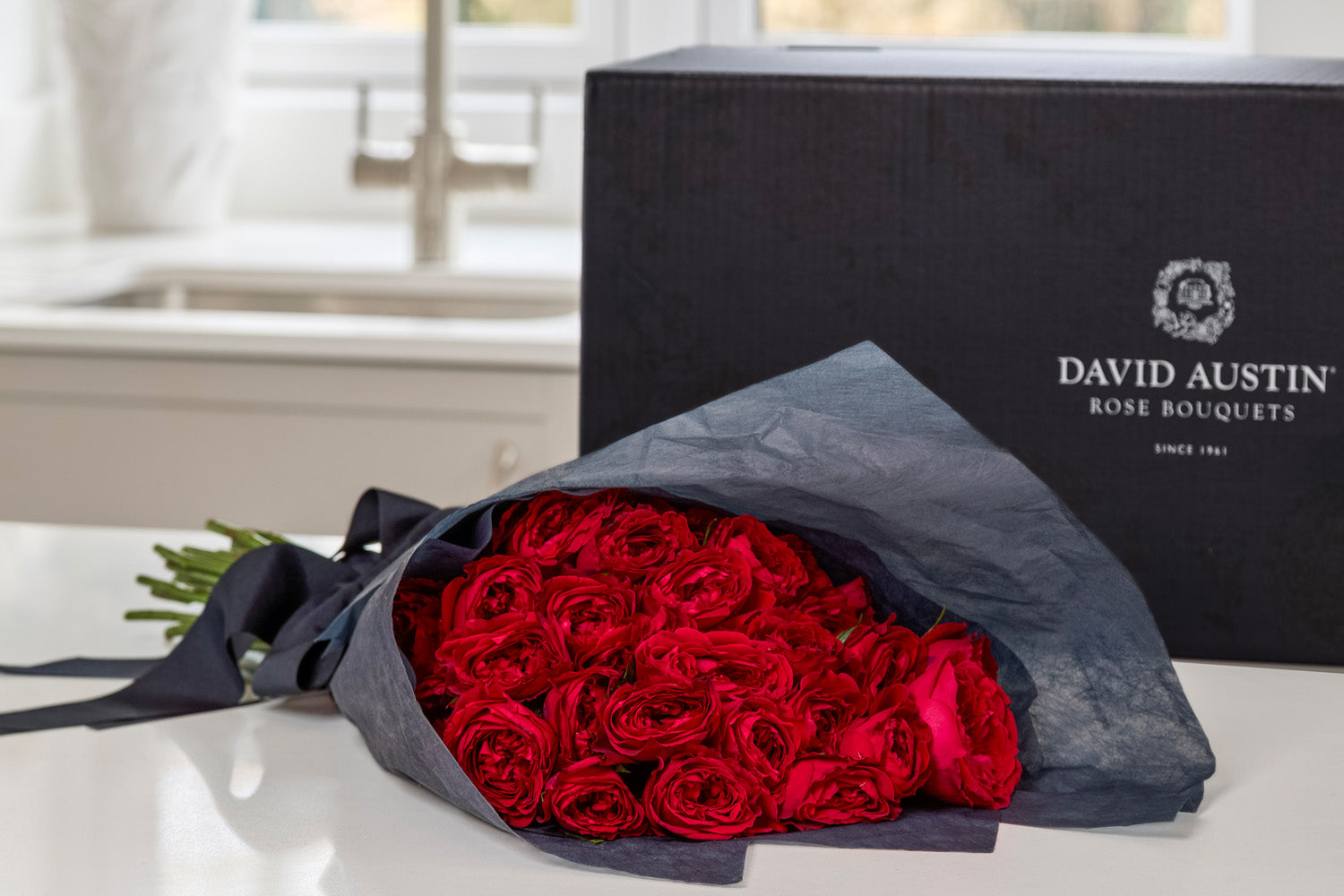 Bouquet of red roses wrapped in midnight blue tissue with luxury gift box